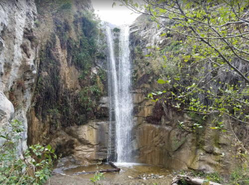 A serene waterfall cascading down rocky cliffs, surrounded by lush greenery and a tranquil pool below.