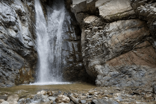 A waterfall cascades down rocky cliffs into a small pool, surrounded by rugged stone formations.