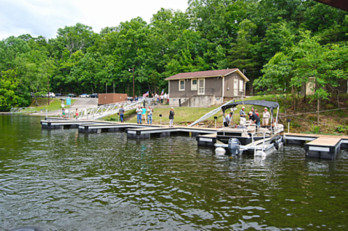 A lakeside scene with a dock, a house, and people enjoying the outdoors among trees and water.