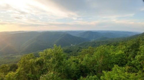 A panoramic view of rolling green mountains under a soft, cloudy sky at sunset.