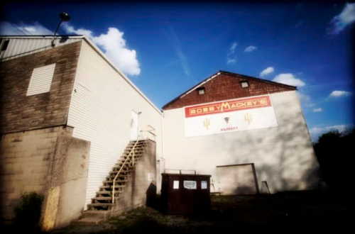 Exterior view of a building with a sign reading "Bobby Mackey's Music World," featuring stairs and a dumpster nearby.