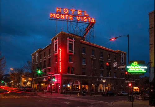 Historic Hotel Monte Vista illuminated at dusk, featuring neon signs and a bustling street scene.