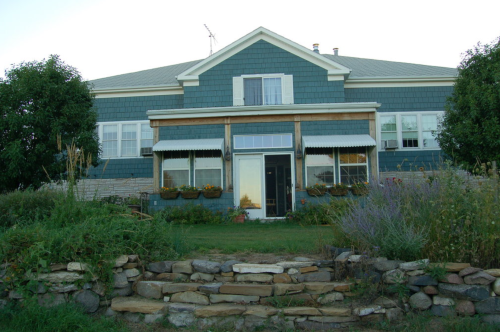 A blue house with a front porch, surrounded by greenery and stone steps leading up to it.