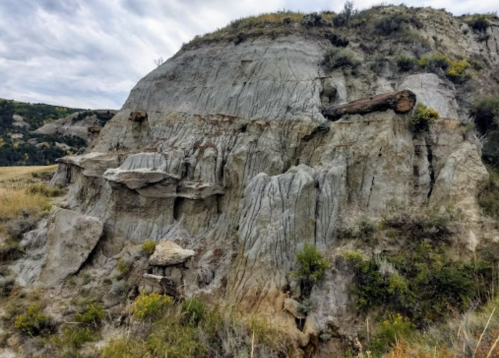 A rugged hillside with layered rock formations and sparse vegetation under a cloudy sky.