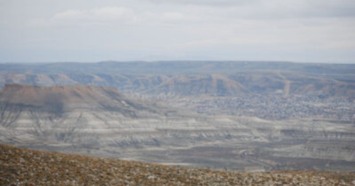 A panoramic view of rugged mountains and valleys under a cloudy sky, showcasing a vast, arid landscape.