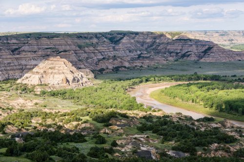 A scenic view of layered hills and a winding river surrounded by lush greenery under a partly cloudy sky.
