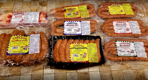 Various packages of Conecuh sausage products displayed on a tiled surface, including bacon and different sausage types.