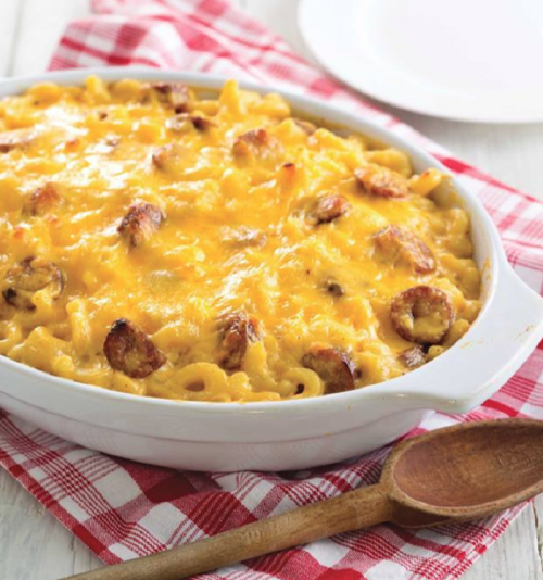 A creamy baked macaroni and cheese dish topped with melted cheese and sausage, served in a white casserole dish.
