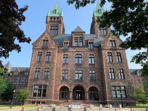 Historic building with stone facade and green-tipped towers, surrounded by trees and a clear blue sky.