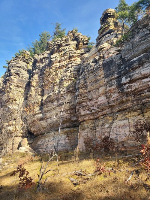 Rocky cliffside with layered stone formations and sparse vegetation under a clear blue sky.