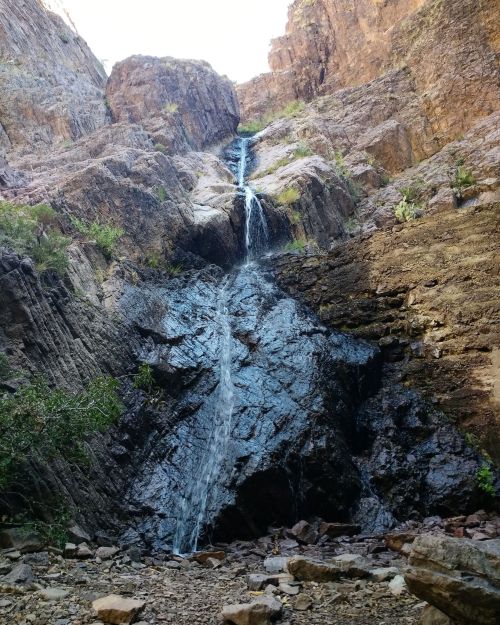 A waterfall cascading down rocky cliffs surrounded by rugged terrain and sparse vegetation.