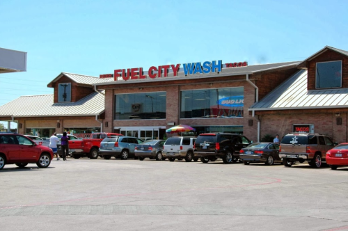 A busy car wash and convenience store with multiple vehicles parked outside under a clear blue sky.