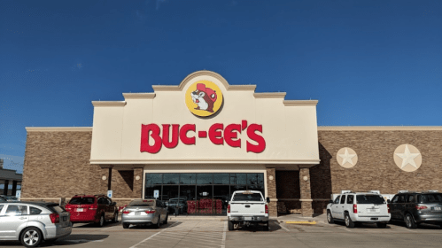 Exterior of a Buc-ee's convenience store with a clear blue sky and parked cars in front.