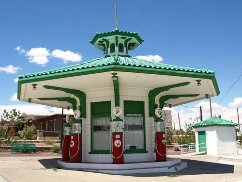 A vintage gas station with a green and white design, featuring multiple gas pumps and a unique roof structure.
