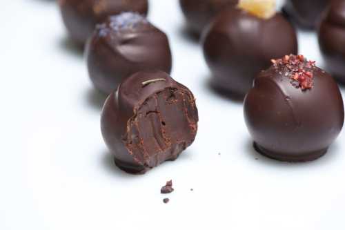 A close-up of chocolate truffles, one partially bitten, showcasing a rich, creamy filling and various toppings.