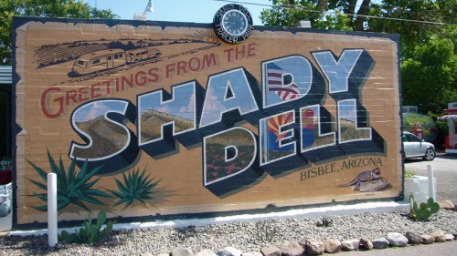 Colorful mural reading "Greetings from the Shady Dell" in Bisbee, Arizona, featuring desert plants and a vintage trailer.