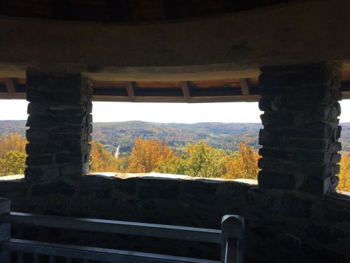 View from a stone lookout tower, showcasing a colorful autumn landscape with rolling hills and trees.