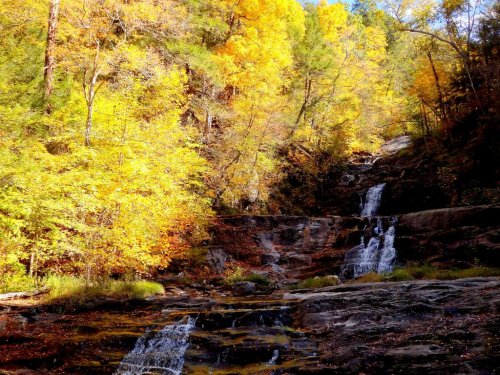 A serene waterfall cascades down rocky terrain, surrounded by vibrant autumn foliage in shades of yellow and orange.