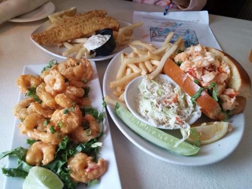 A plate of fried shrimp, a fish fillet, fries, a shrimp sandwich, coleslaw, and a lemon wedge on a table.