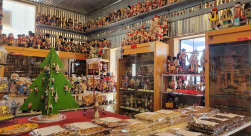 A festive shop filled with nutcracker figurines, a green Christmas tree, and various treats displayed on tables.