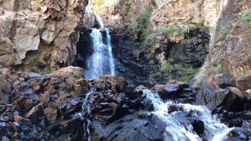 A scenic waterfall cascading over rocky cliffs, surrounded by lush greenery and rugged terrain.