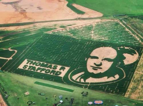 Aerial view of a corn maze featuring a large portrait of Thomas P. Stafford, surrounded by green fields.