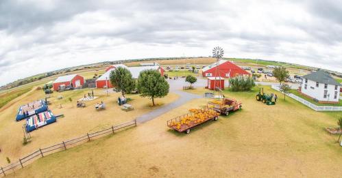 Aerial view of a farm with red barns, a windmill, and various farm equipment on a cloudy day.