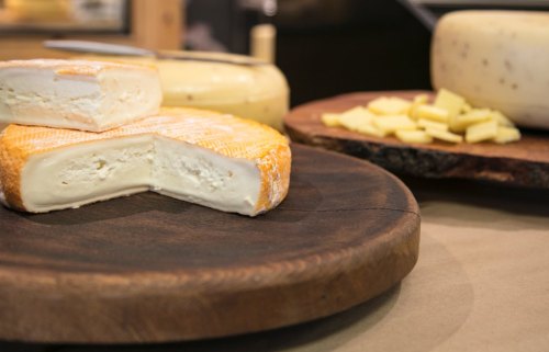 A wooden platter with various cheeses, including a round cheese cut in half, and small cheese cubes on the side.