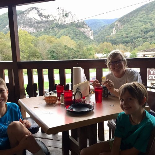 A family enjoys a meal on a porch with a scenic mountain view in the background.