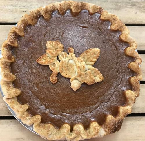 A freshly baked pumpkin pie with a decorative crust and a leaf-shaped topping on a wooden surface.