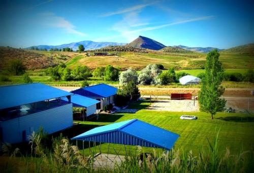 A scenic view of a rural landscape featuring blue-roofed buildings, green fields, and distant mountains under a clear sky.