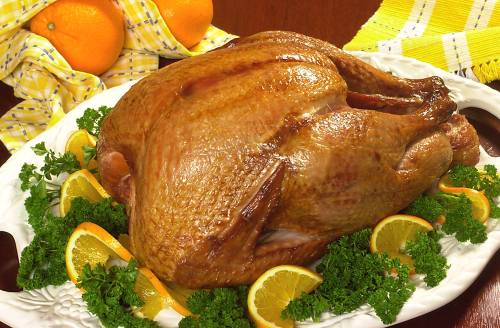 A golden-brown roasted turkey garnished with parsley and orange slices on a white platter, with a yellow checkered cloth in the background.