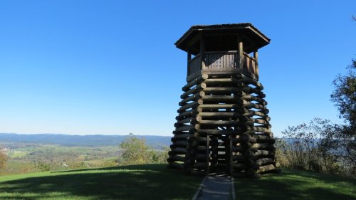 A wooden observation tower on a grassy hill, overlooking a scenic valley and blue sky.