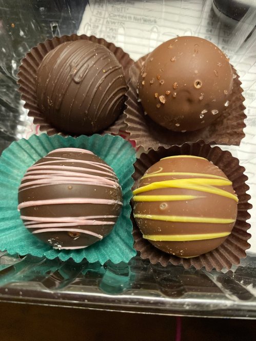 Four assorted chocolate truffles in colorful paper cups, featuring dark and milk chocolate with various toppings and designs.