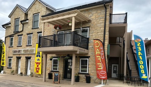A stone building with a balcony, featuring colorful banners for a café and seafood, set in a small town.