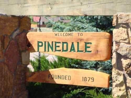 Wooden sign reading "Welcome to Pinedale" with "Founded 1879" below, surrounded by greenery and stone.