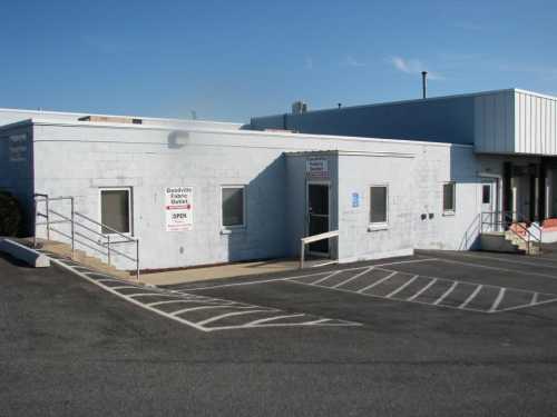 A light blue building with a ramp and parking spaces, featuring signs indicating it is open for business.