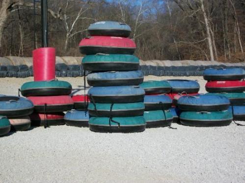 A stack of colorful inflatable tubes on a gravel surface, with trees and a blue sky in the background.