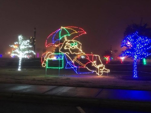 A colorful light display featuring a figure lounging under an umbrella, surrounded by illuminated trees.