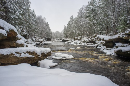 A snowy river scene with rocky banks and trees, creating a serene winter landscape.