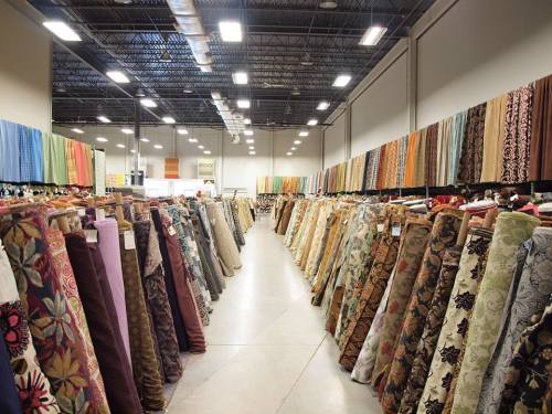 A spacious fabric store aisle lined with colorful rolls of various patterned fabrics on display.