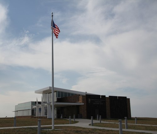 Modern building with large windows, featuring a flagpole with an American flag, set against a cloudy sky.
