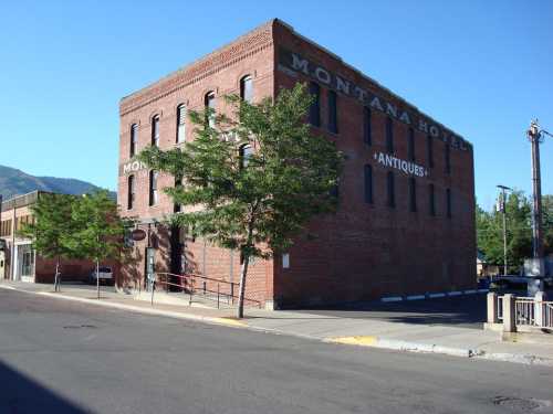 Historic brick building labeled "Montana Hotel" with trees and a clear blue sky in the background.