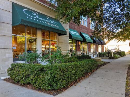 A sidewalk lined with greenery in front of a brick building featuring shops with green awnings.