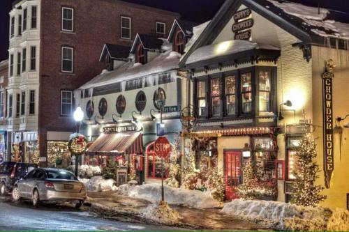 A snowy street scene at night featuring festive buildings, including a chowder house and a restaurant, adorned with holiday decorations.