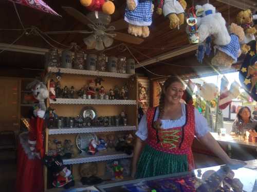 A woman in traditional attire stands at a festive booth decorated with toys and ornaments, smiling at the camera.