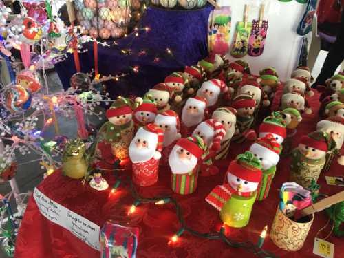 A festive display of handmade holiday decorations, including Santa and snowman figures, on a red tablecloth.