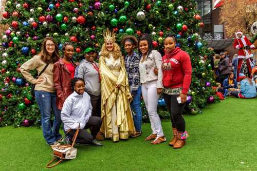 A group of eight people poses together in front of a decorated Christmas tree, smiling and celebrating the holiday season.