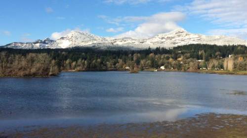 A serene lake surrounded by snow-capped mountains and lush trees under a clear blue sky.