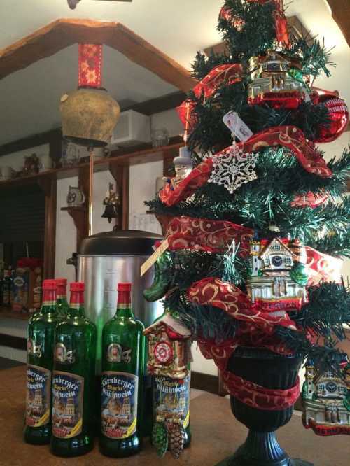 A decorated Christmas tree with ornaments beside three green bottles of herbal liqueur on a table.